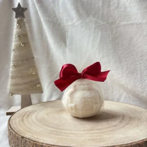 Świeca sojowa w kształcie świątecznej bombki, zapakowana w tiul z czerwoną kokardą.