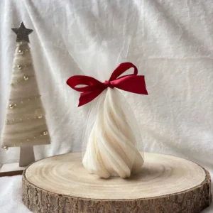 Świeca sojowa w kształcie choinki, zapakowana w biały tiul z czerwoną wstążką.