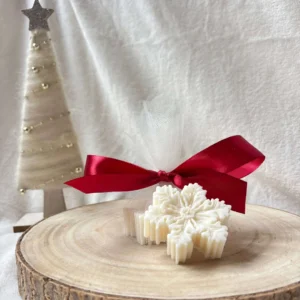 Dwie świece sojowe w kształcie gwiazdek, jedna zapakowana w tiul z czerwoną kokardą.