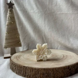 Świeca sojowa w kształcie gwiazdki, ustawiona na drewnianym tle z choinką w tle.