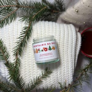Świeca sojowa Mentalnie na Bali położona na białym swetrze z gałązkami świerku i kubkiem herbaty, tworząca przytulny zimowy klimat.