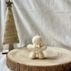 Świeca sojowa w kształcie piernikowego ludzika, ustawiona na drewnianym krążku.