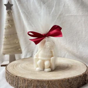 Świeca sojowa w kształcie Świętego Mikołaja, zapakowana w biały tiul z czerwoną kokardą.